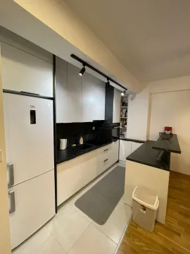 Moderna kuhinja sa bijelim elementima, tamnom radnom površinom i šankom. - image 15