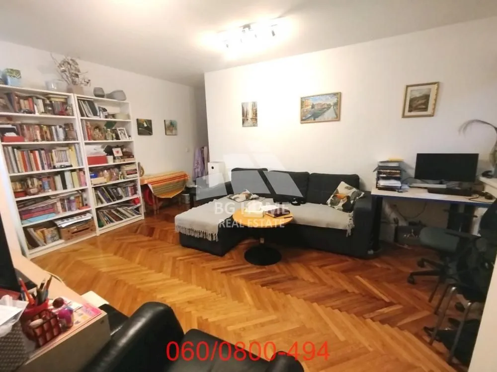 Dnevni boravak sa garniturom, policama za knjige i radnim stolom.