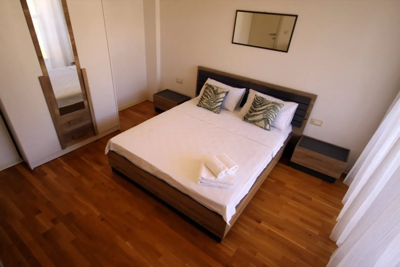 Bright bedroom with a double bed and wooden flooring.