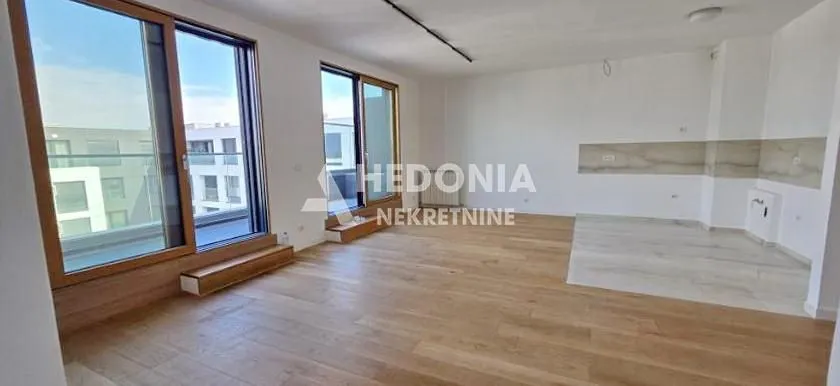 Prostrana prazna dnevna soba sa drvenim podom i velikim balkonskim vratima.