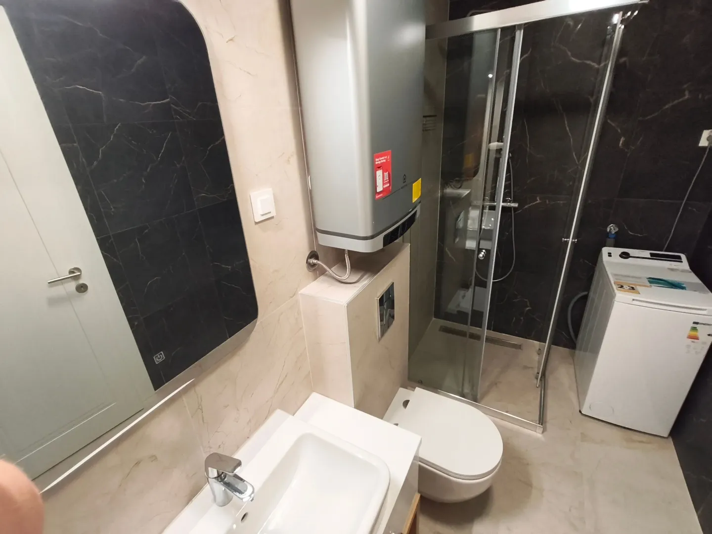 Moderno opremljeno kupatilo sa tuš kabinom, umivaonikom i veš mašinom.