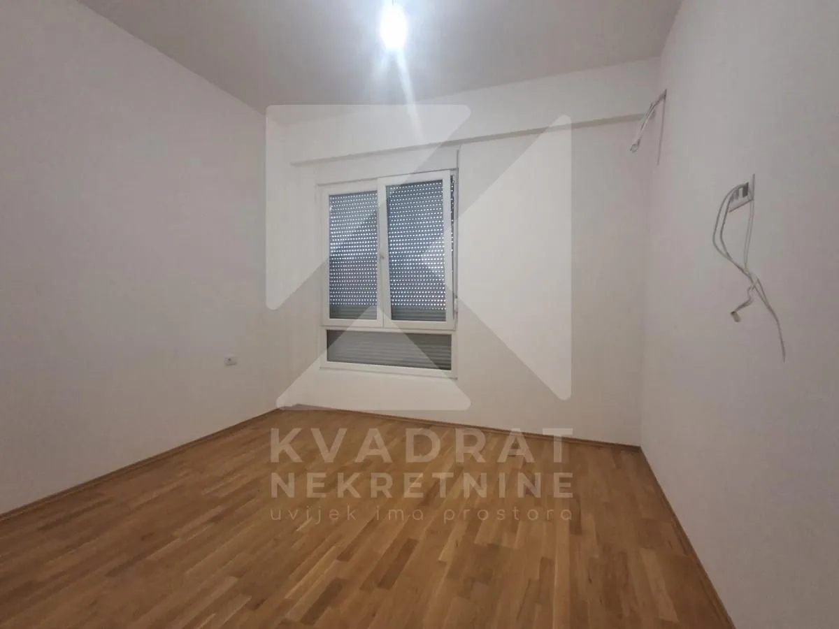 Prazna neopremljena soba sa drvenim podom i prozorom.