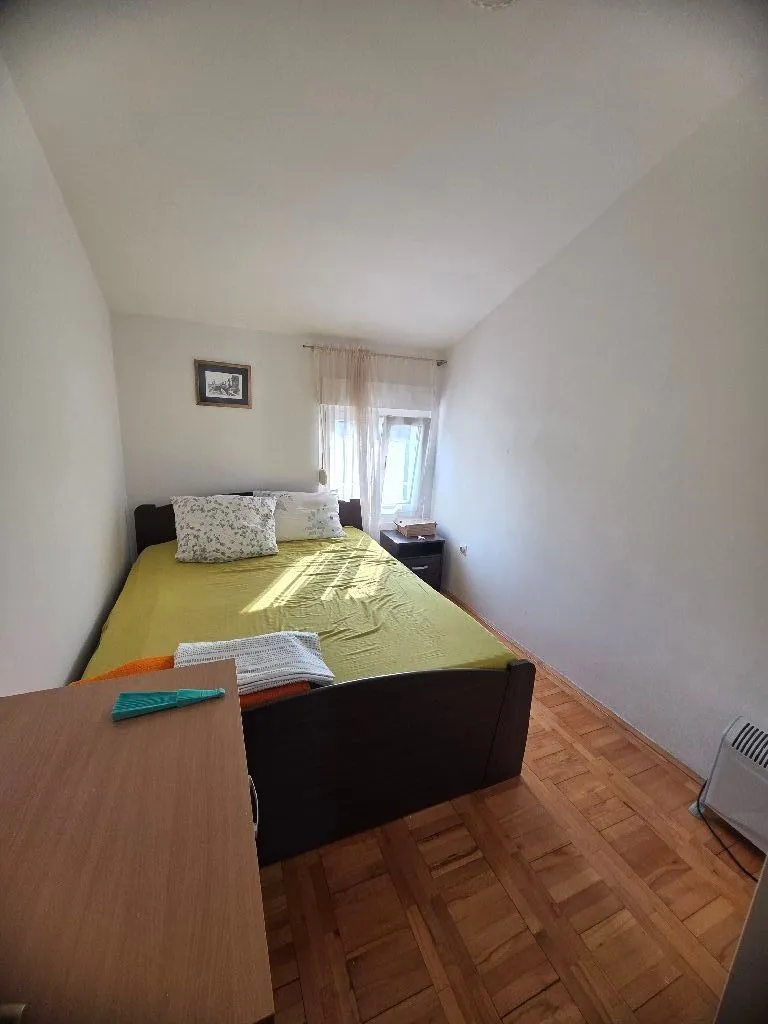Spavaća soba sa bračnim krevetom, drvenim podom i prozorom.