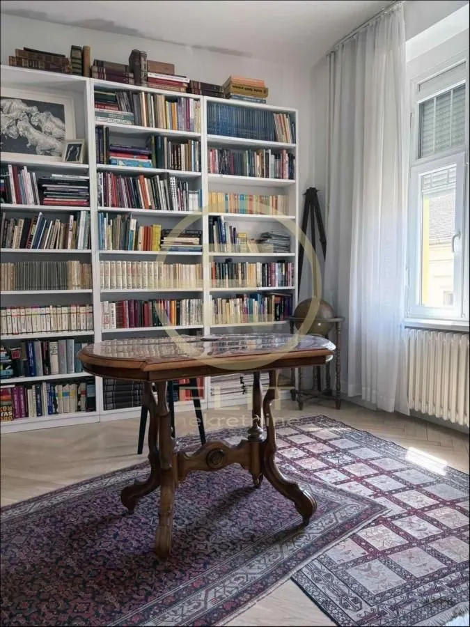 Dnevna soba sa velikom bibliotekom i drvenim stolom.