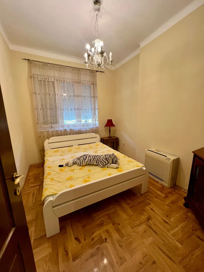 Bedroom with a white bed, parquet flooring, and a chandelier.