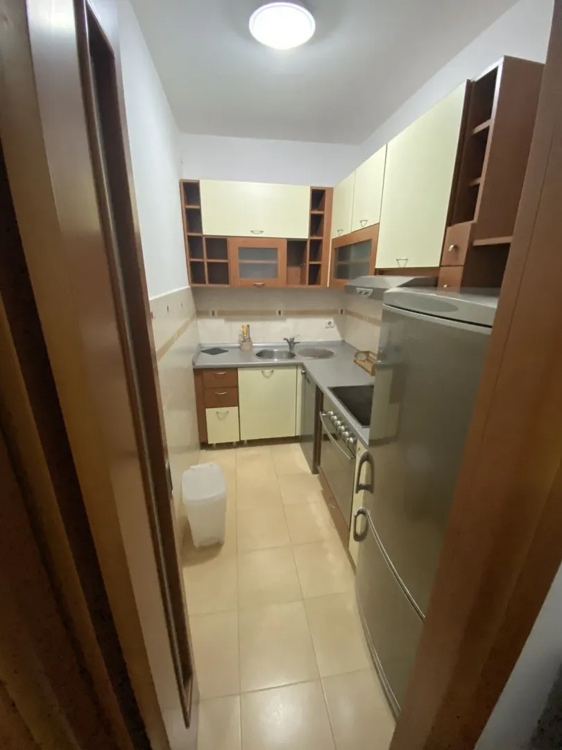 A narrow kitchen with light-colored cabinets and a refrigerator.