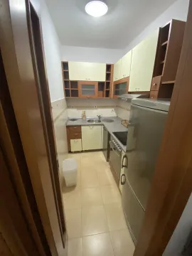 A narrow kitchen with light-colored cabinets and a refrigerator. - image 7