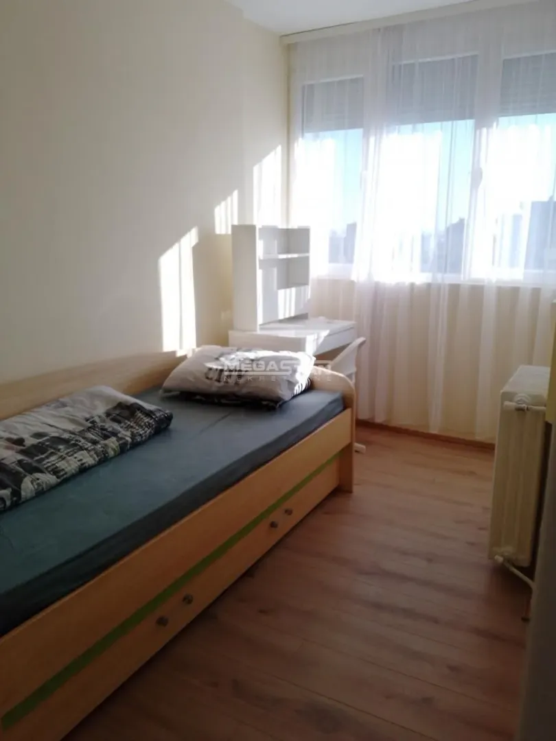 Manja spavaća soba sa krevetom i radnim stolom pored prozora.
