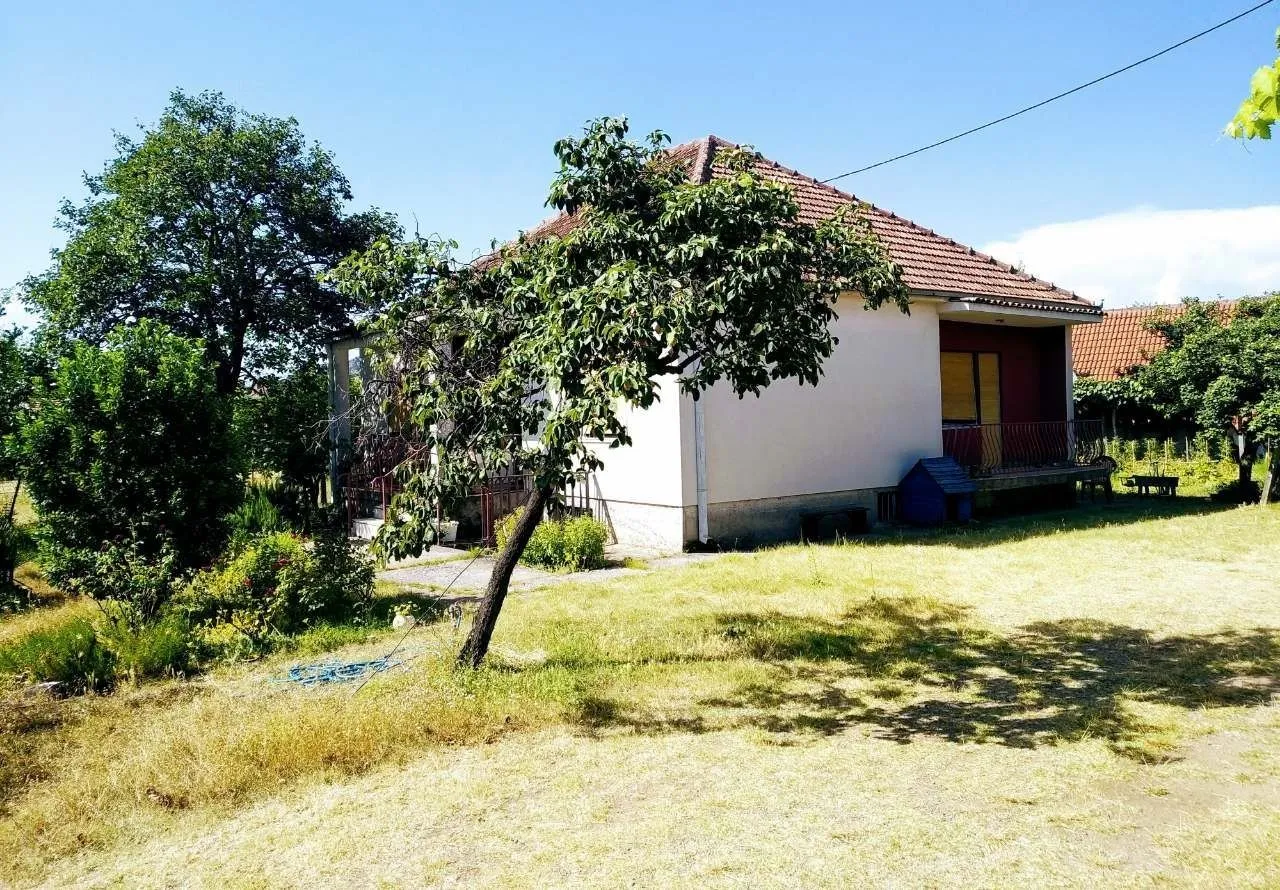 Pogled na kuću sa dvorištem i drvećem.