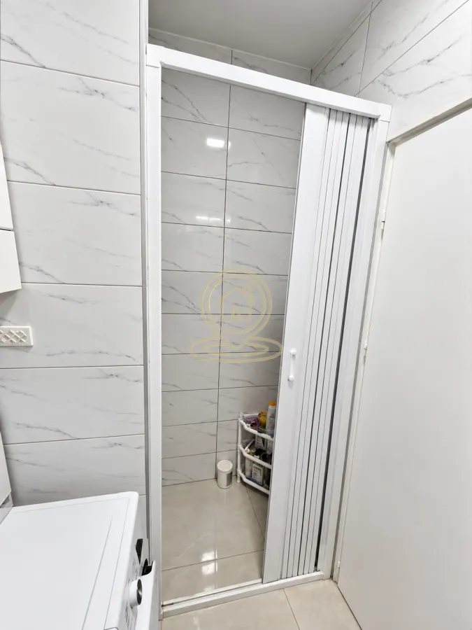 Pogled na kupatilo sa belim pločicama i harmonika vratima.