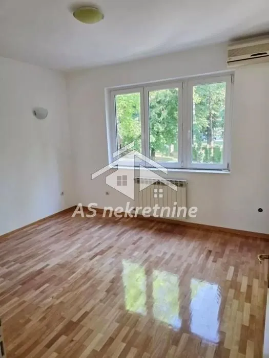 Prazna soba sa parketom, prozorom i klima uređajem.