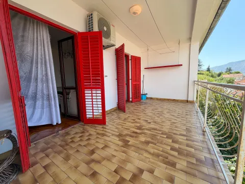 Prostrani popločani balkon sa crvenim kapcima i pogledom na okolinu. - image 2