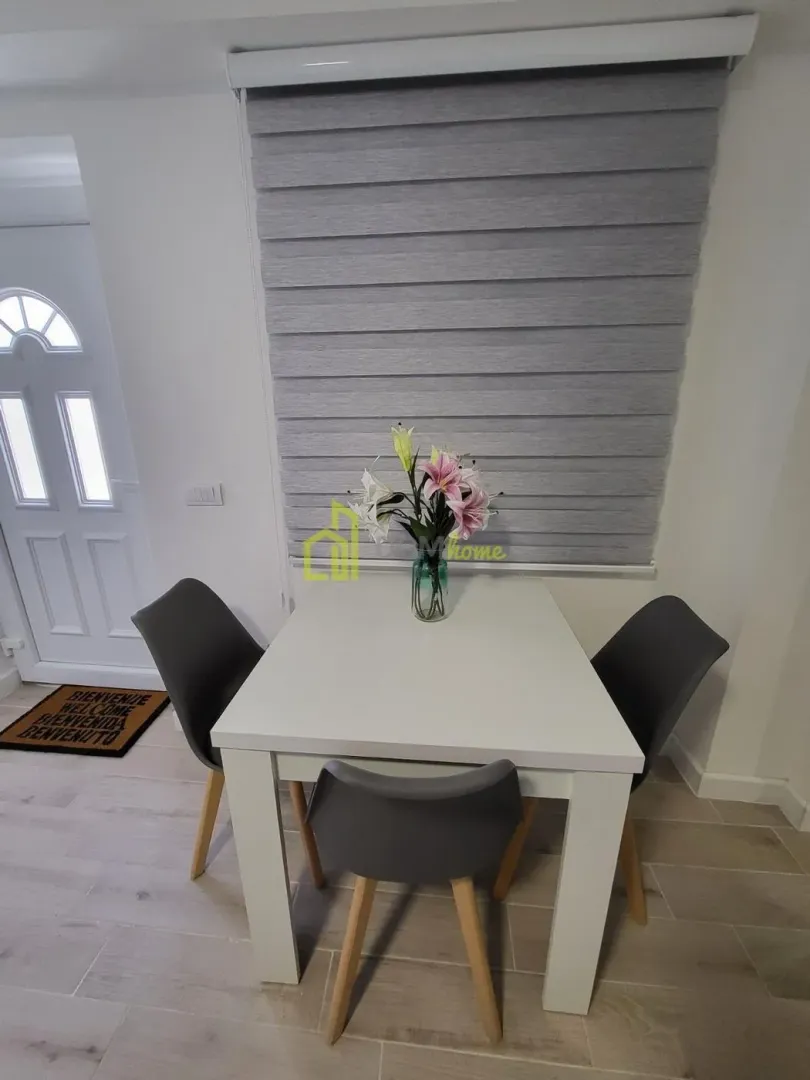 Smaller dining table with three white chairs near the window.