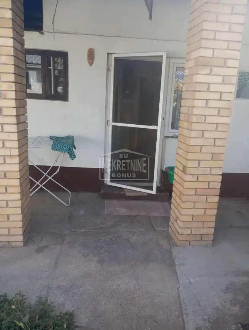 Ulaz u kuću sa natkrivenom terasom i ciglenim stubovima.