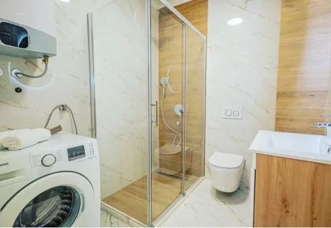 Modern bathroom with a walk-in shower, washbasin, toilet, and washing machine. - image 6