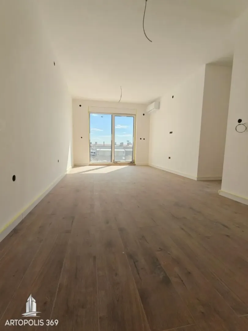 Prazna neopremljena prostorija sa postavljenim parketom i izlazom na terasu.