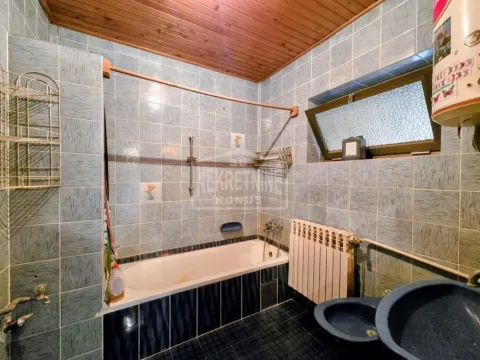 Kupatilo obloženo pločicama sa kadom i drvenim plafonom. - image 10