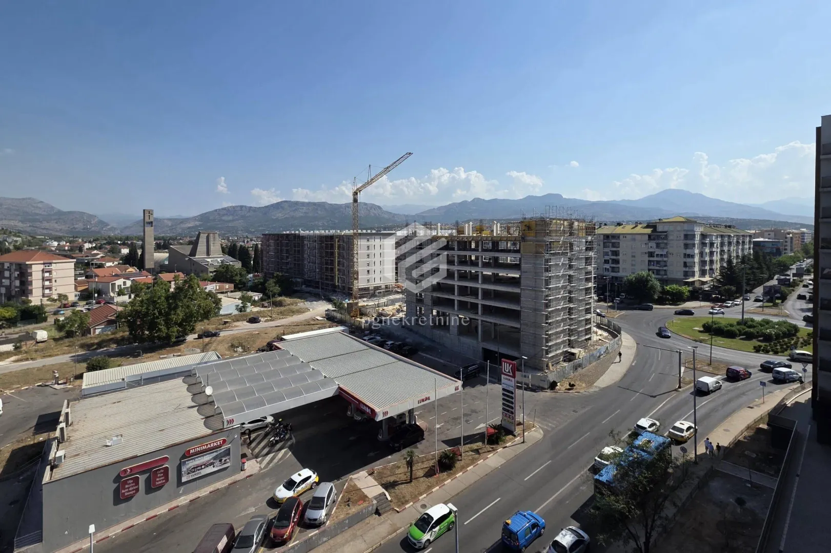 View from the window showing surrounding buildings, a construction site, and mountains in the distance.