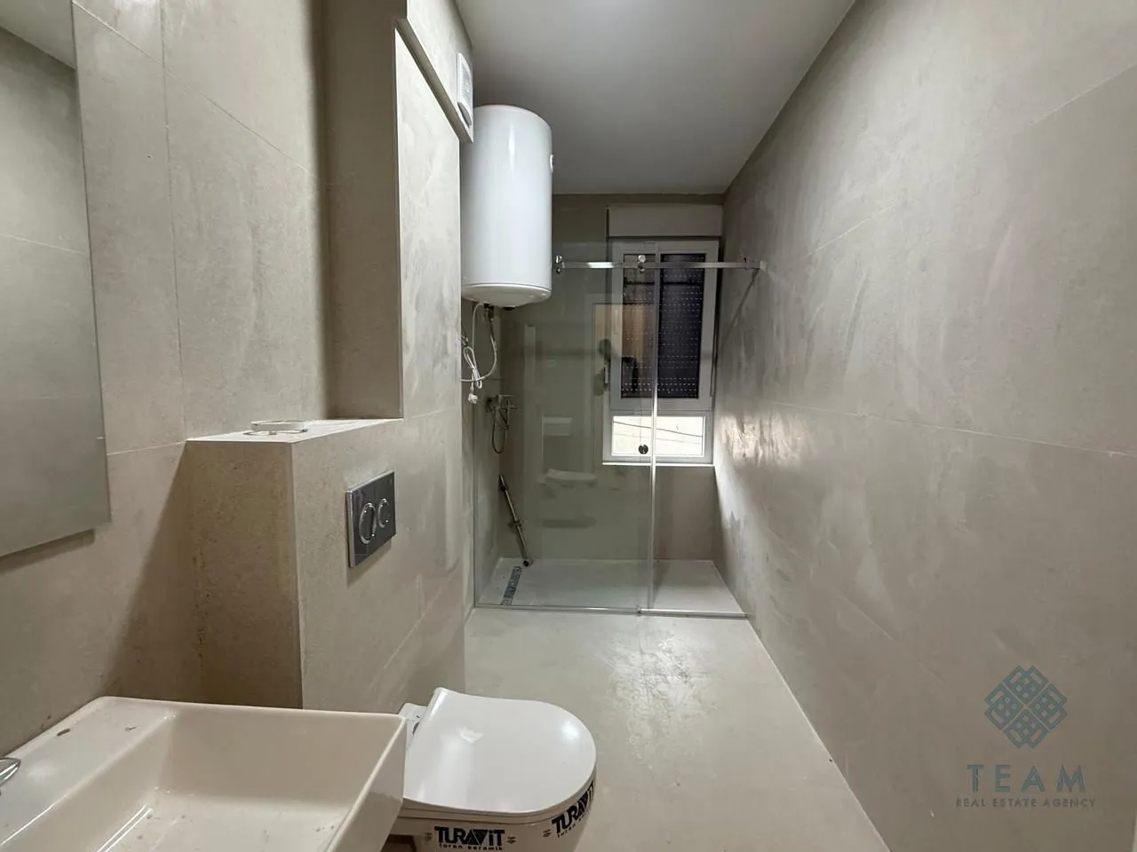 Savremeno opremljeno kupatilo sa tuš kabinom, umivaonikom i wc šoljom u bež tonovima.