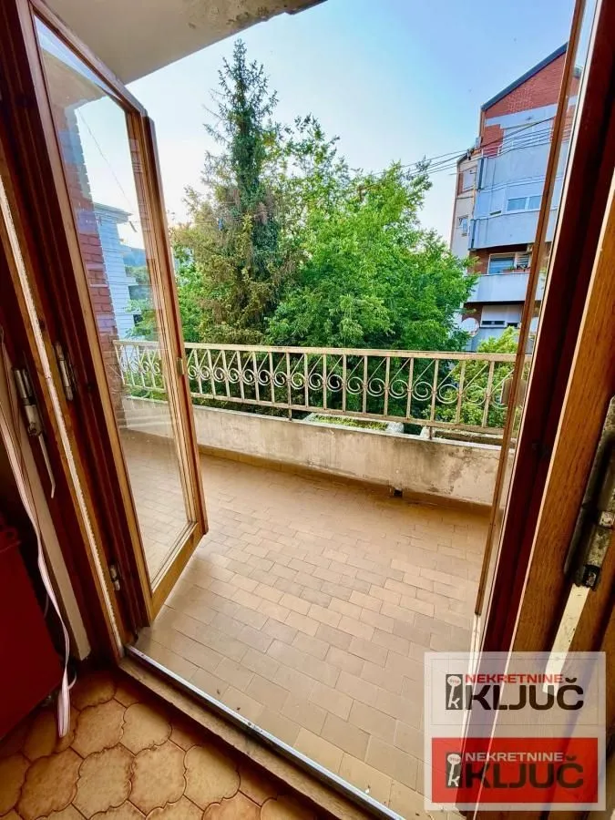 Manji popločani balkon sa metalnom ogradom i pogledom na zelenilo.