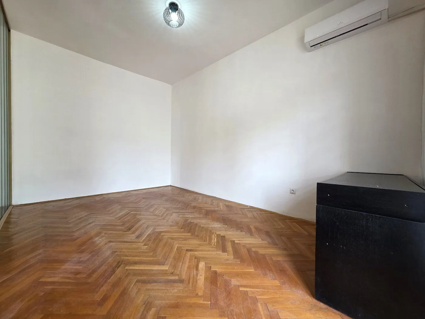 Empty room with parquet flooring and an air conditioning unit.