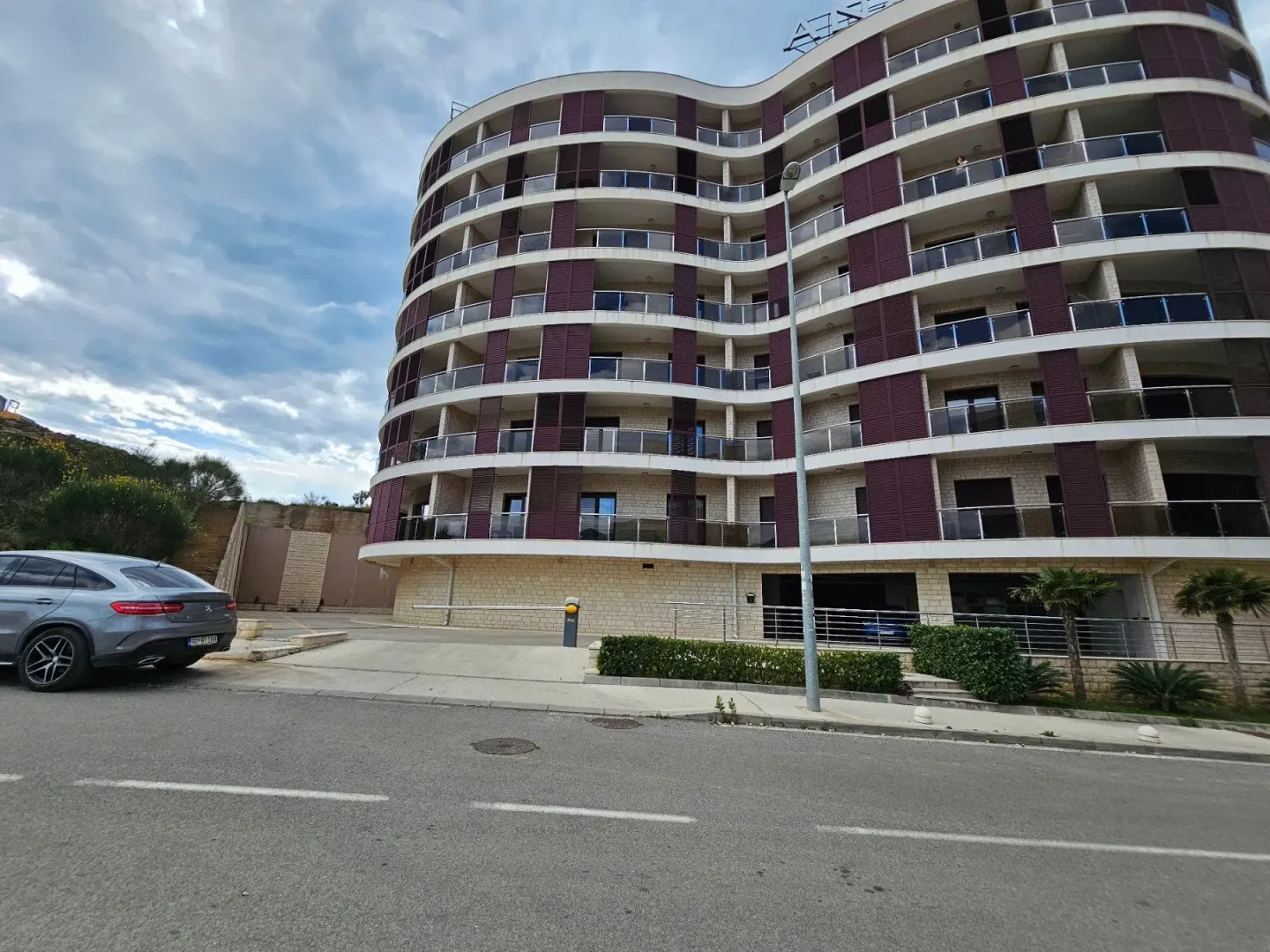 View of a modern residential building with balconies and a parking area in front.