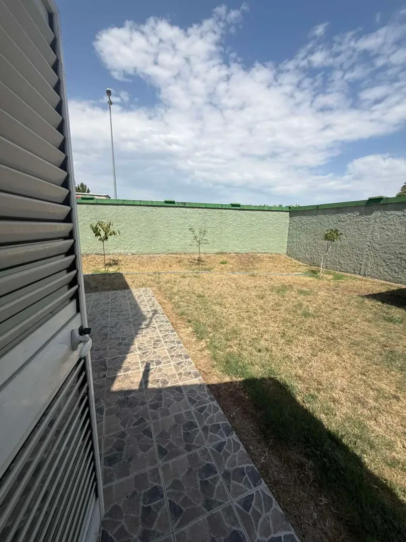 Pogled na dvorište i popločanu terasu sa ogradom.