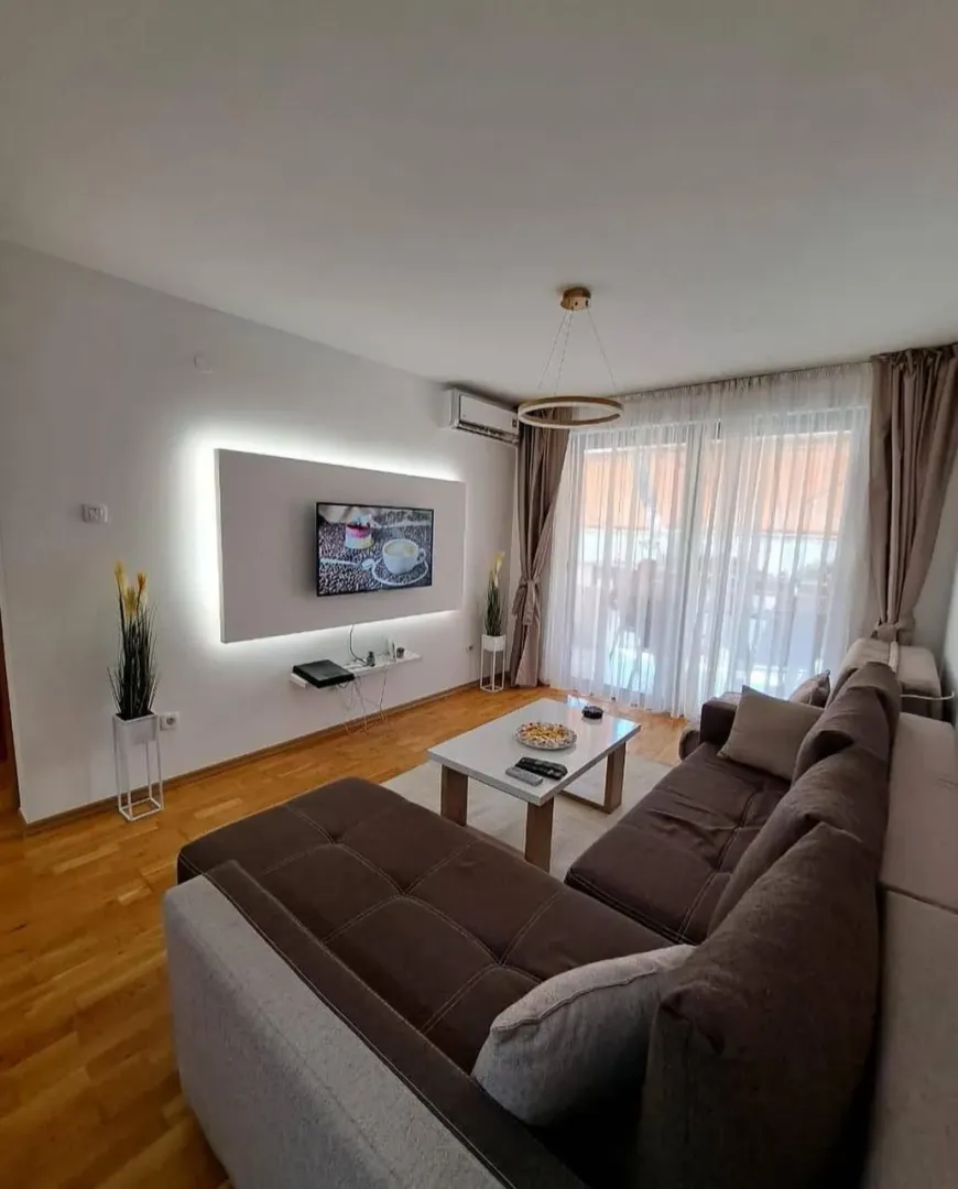 Dnevna soba sa ugaonom garniturom, televizorom i izlazom na terasu.