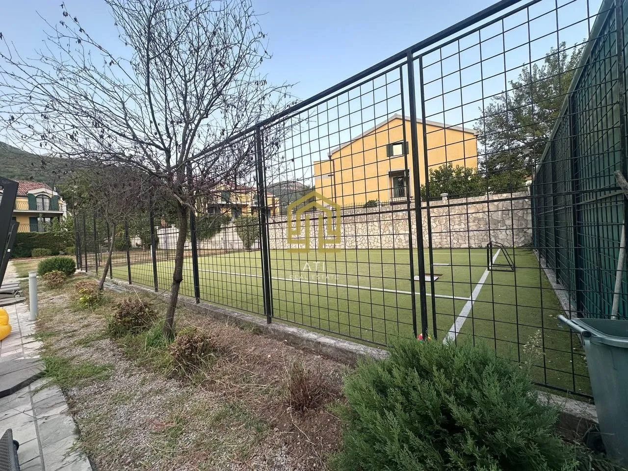 Ograđeni sportski teren sa vještačkom travom.