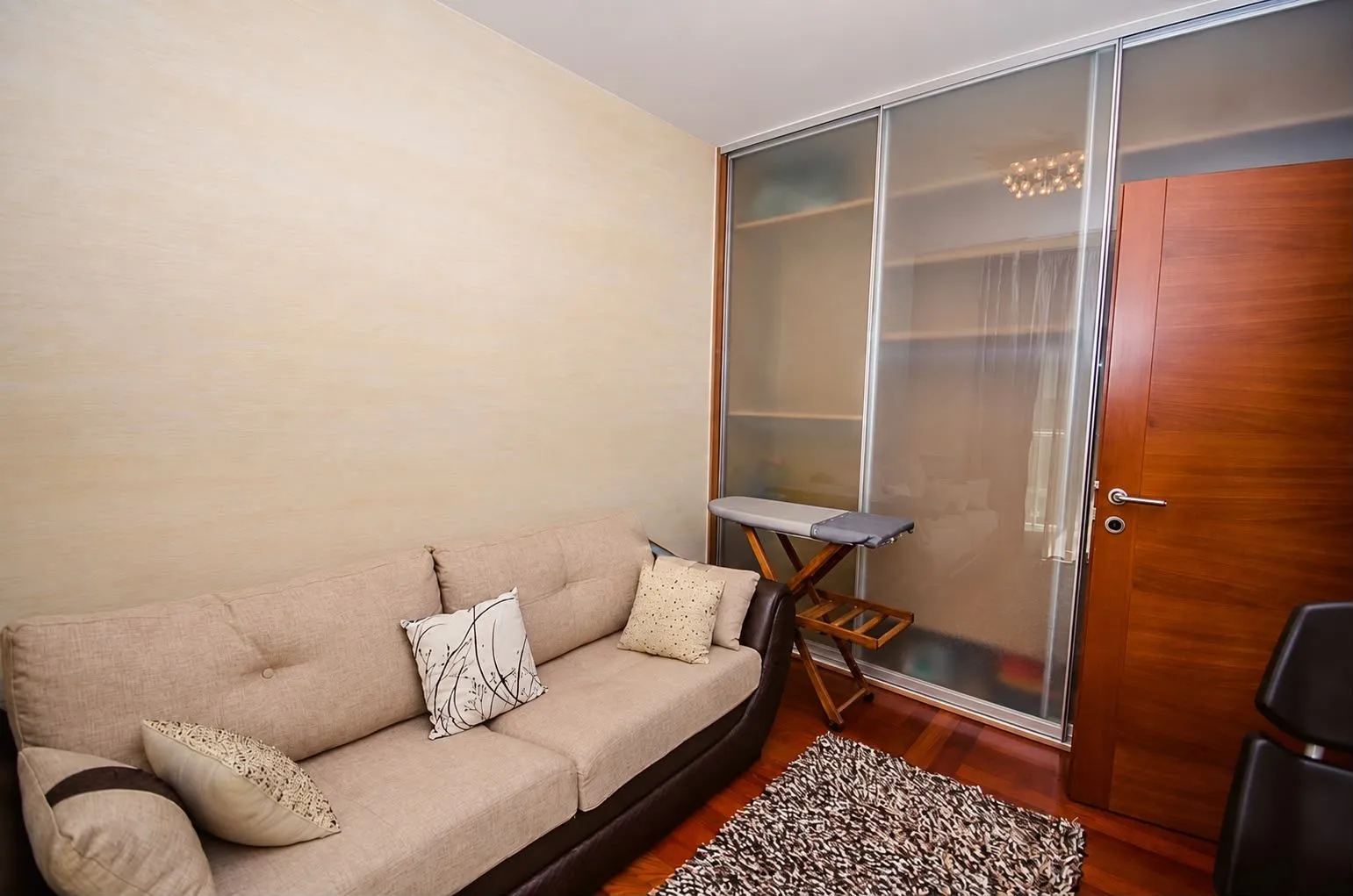 Living room with a beige sofa, built-in wardrobe, and wooden door.