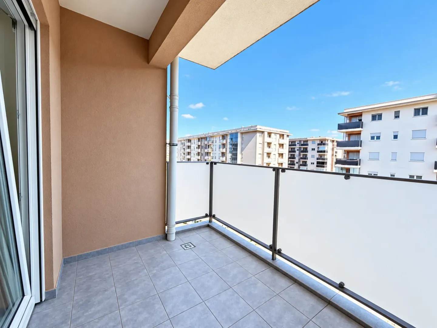 Empty tiled balcony with a glass railing and a view of surrounding buildings.