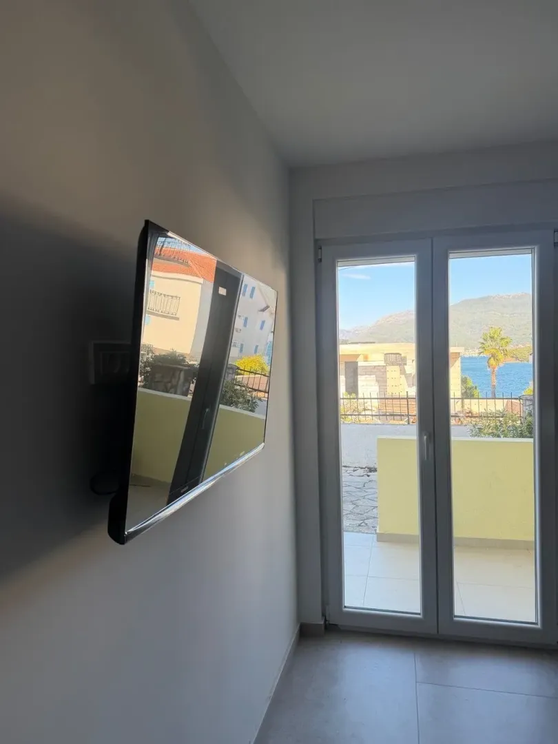 Dnevni boravak sa televizorom na zidu i izlazom na terasu sa pogledom na more.