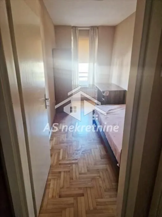 Smaller bedroom with a bed, wardrobe, and wooden parquet flooring.