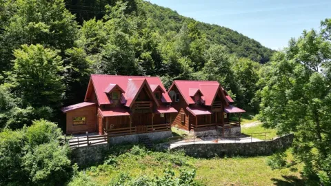 Pogled na drvene vikendice sa crvenim krovom okružene šumom. - image 9