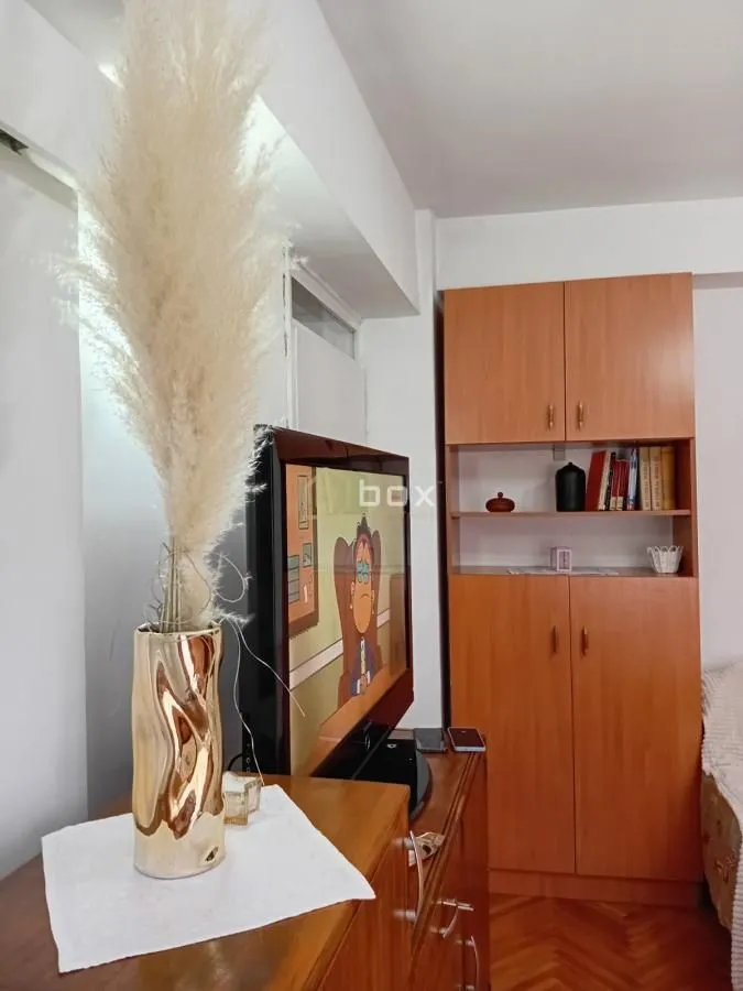 Pogled na deo dnevne sobe sa TV-om, dekorativnom vazom i drvenim ormarom.