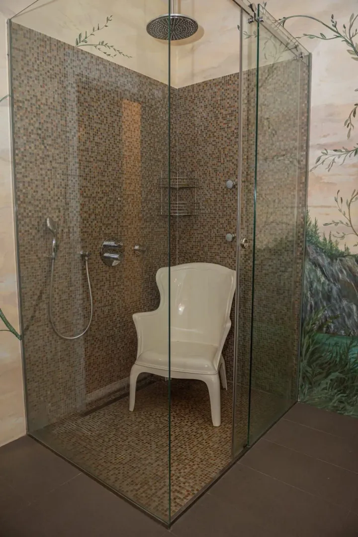 Modern walk-in shower with glass partition and mosaic tiles.