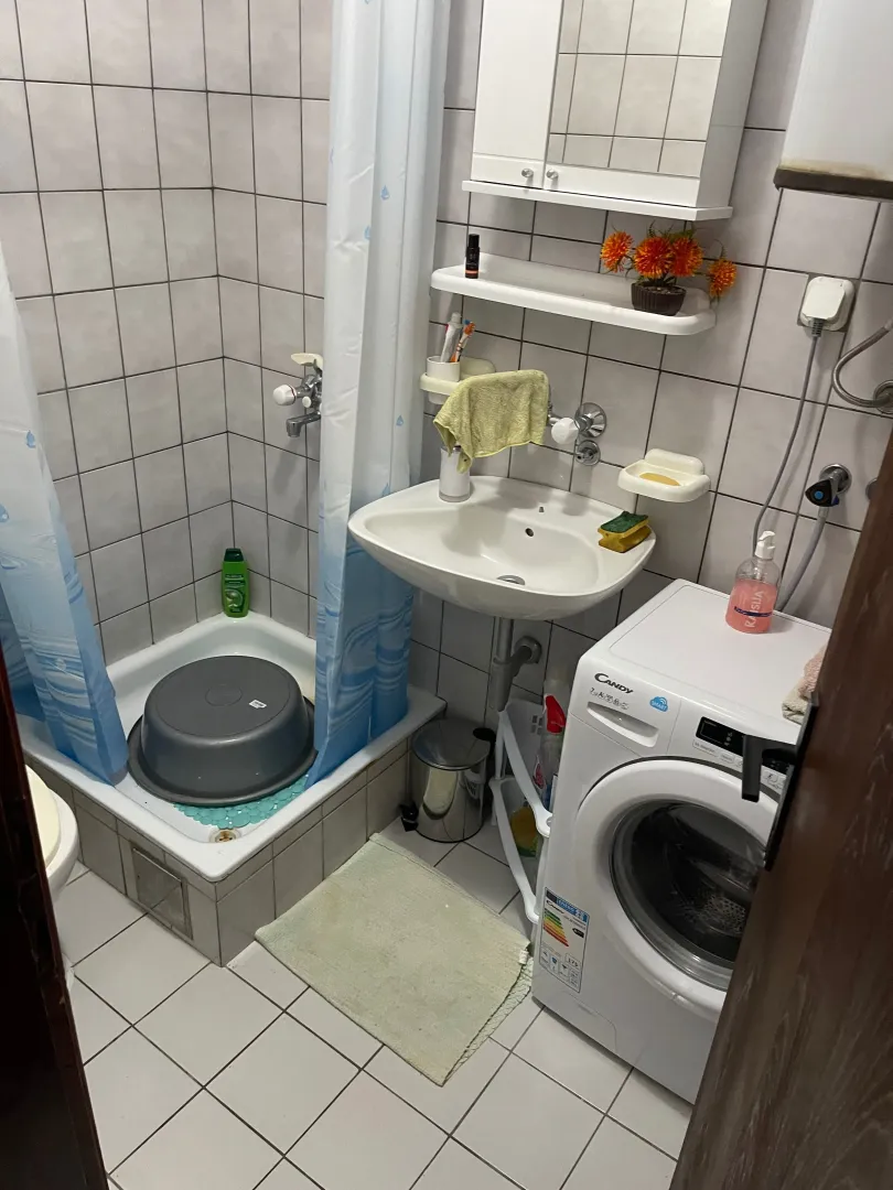 Manje kupatilo sa tuš kabinom, umivaonikom i veš mašinom.