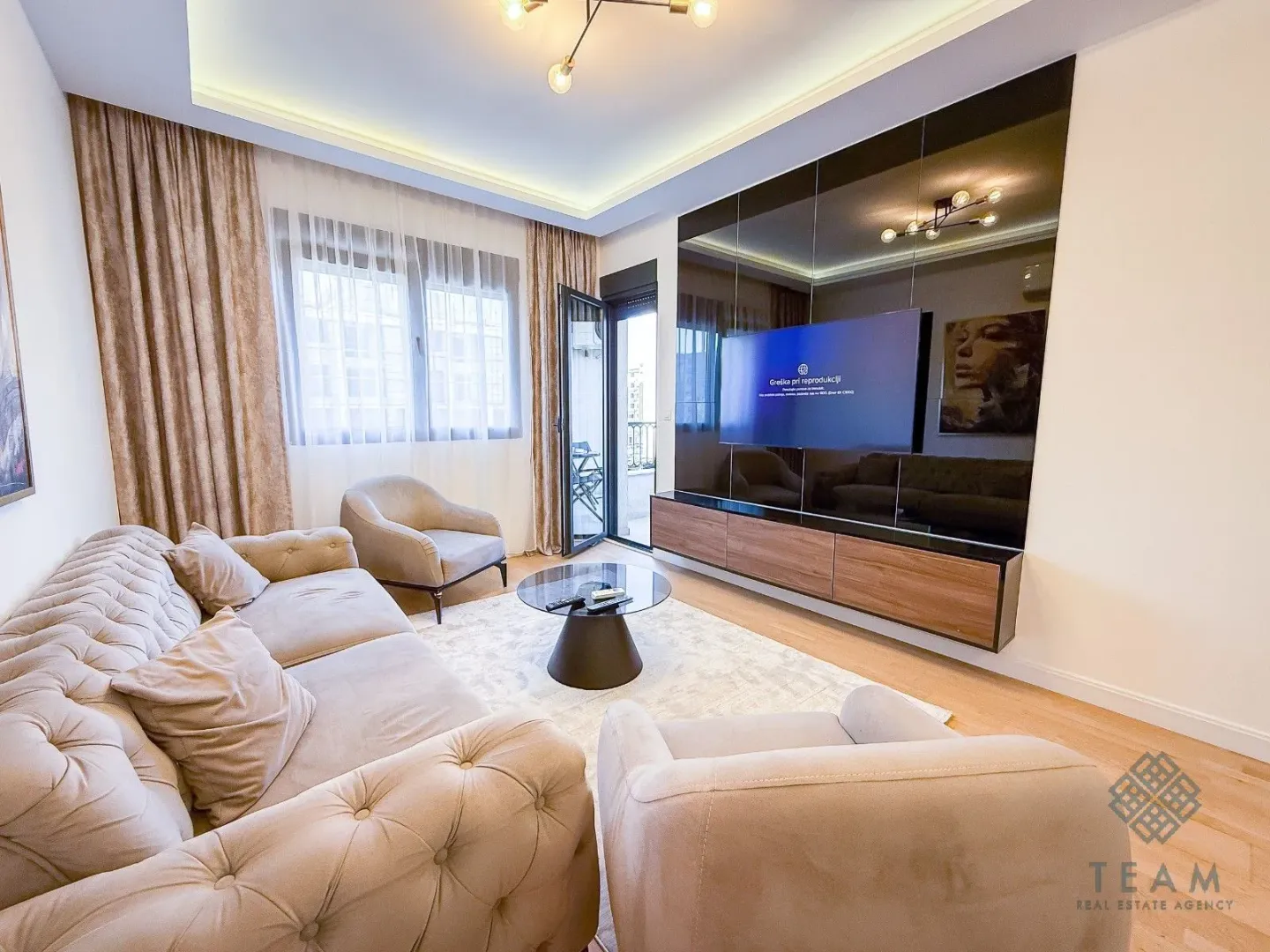 Modern living room with a sofa, armchairs, coffee table and a wall-mounted TV.