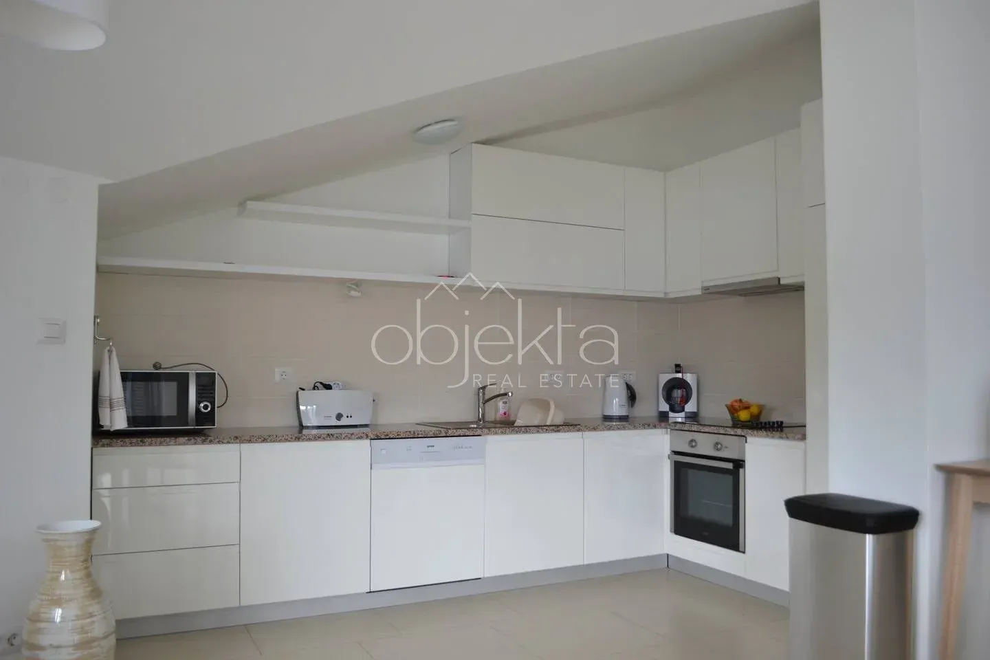 White L-shaped kitchen with built-in appliances and a sloped ceiling.