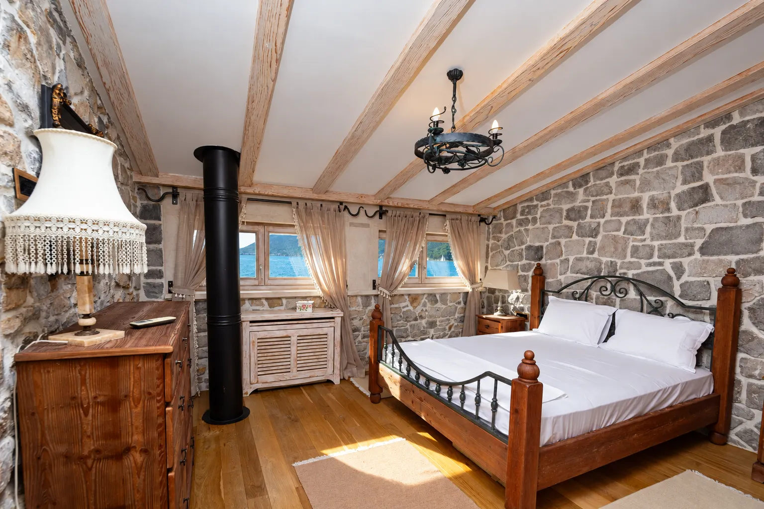 Rustic bedroom with stone walls, wooden ceiling beams, and a double bed.