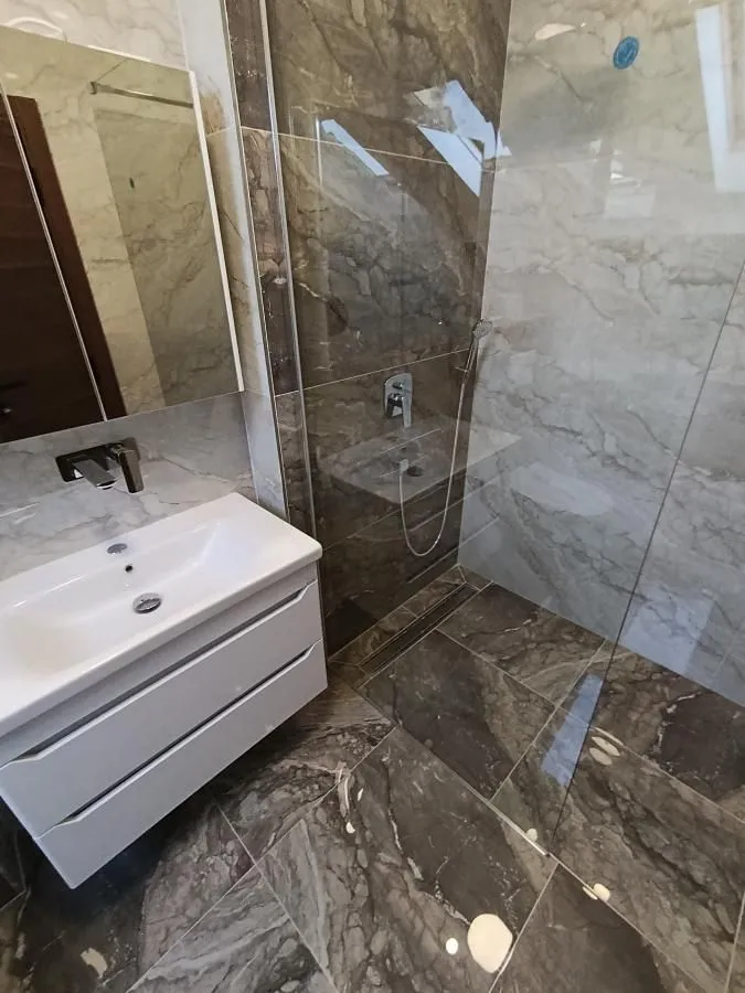 Moderno opremljeno kupatilo sa umivaonikom i tuš kabinom obloženom keramikom.