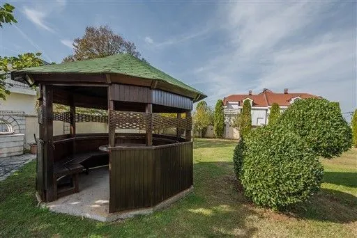 A wooden gazebo in a spacious green yard.