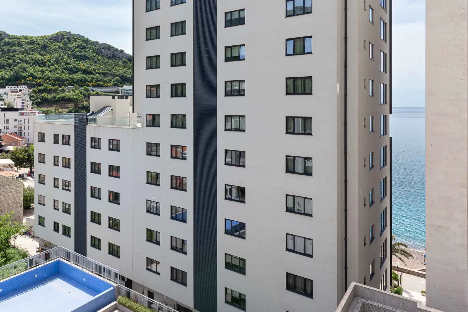 Pogled na spoljašnjost moderne stambene zgrade sa bazenom i pogledom na more.