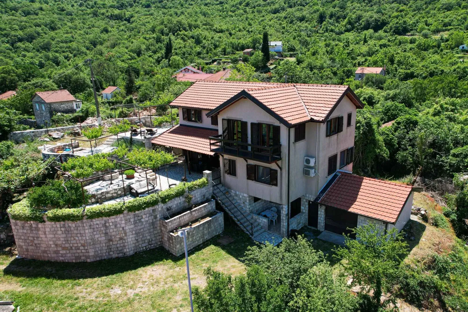 Pogled iz vazduha na dvospratnu kuću sa popločanim dvorištem i okolnim zelenilom.