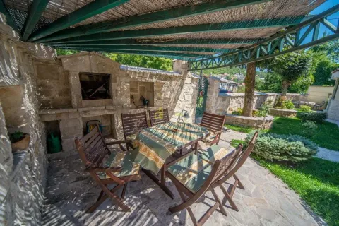 Covered backyard area with a stone BBQ, table, and wooden chairs. - image 7