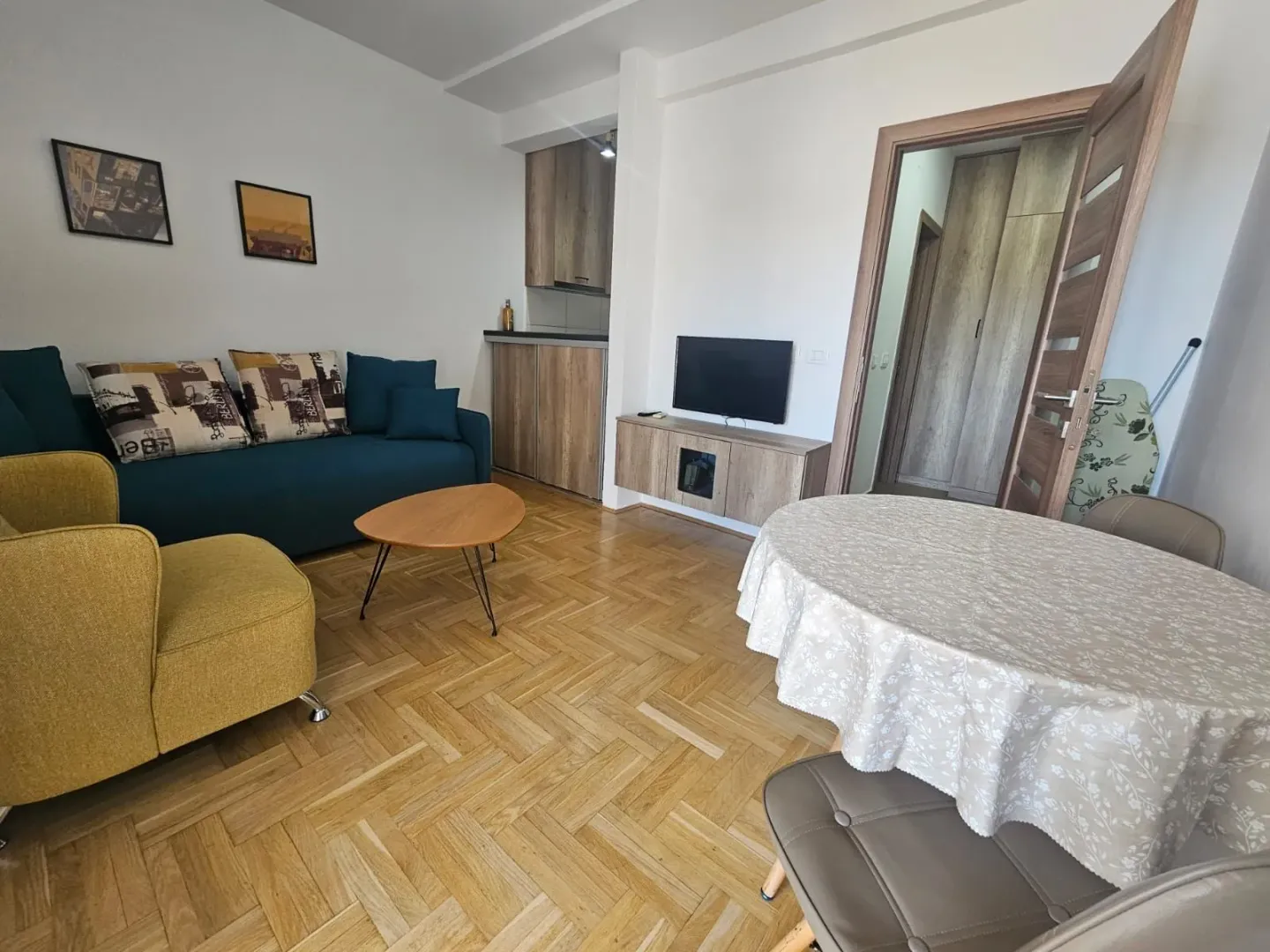 Dnevna soba sa garniturom, trpezarijskim stolom i kuhinjskim elementima u pozadini.
