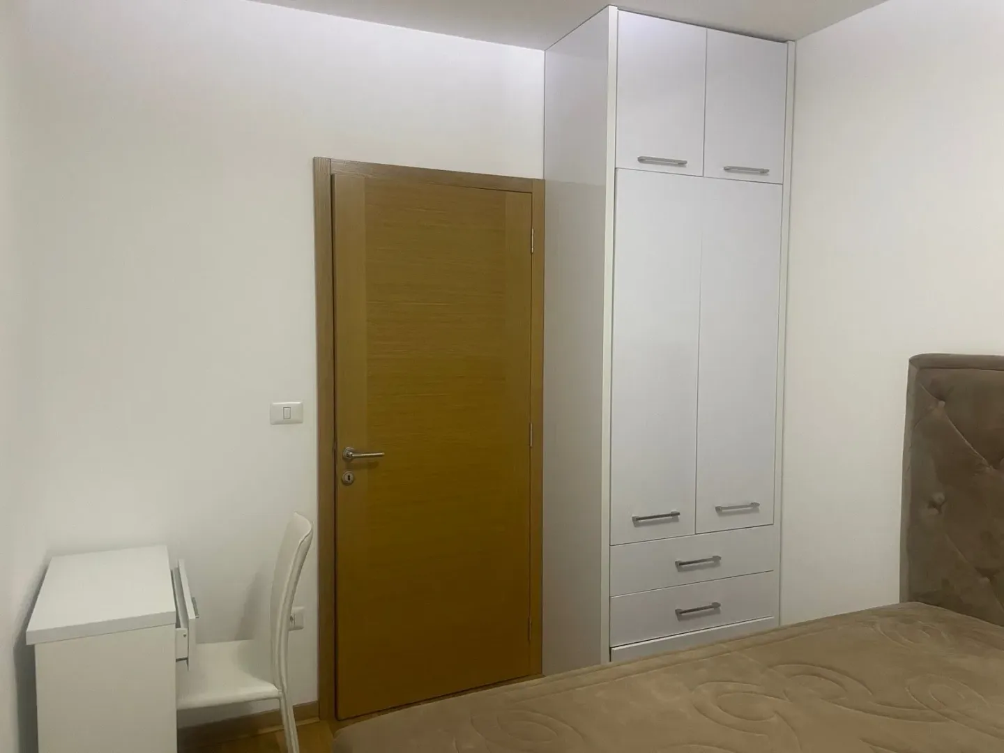 Bedroom with a double bed, white wardrobe, desk, and wooden door.
