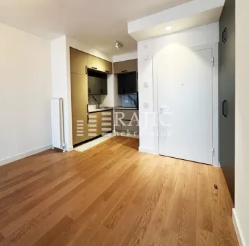 Living room with a view of the entrance door and a small kitchen. - image 4
