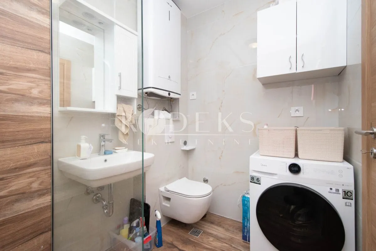 Modern bathroom with a sink, toilet, walk-in shower, and washing machine.