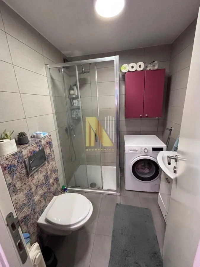 Kompaktno kupatilo sa tuš kabinom, veš mašinom i sanitarijama.